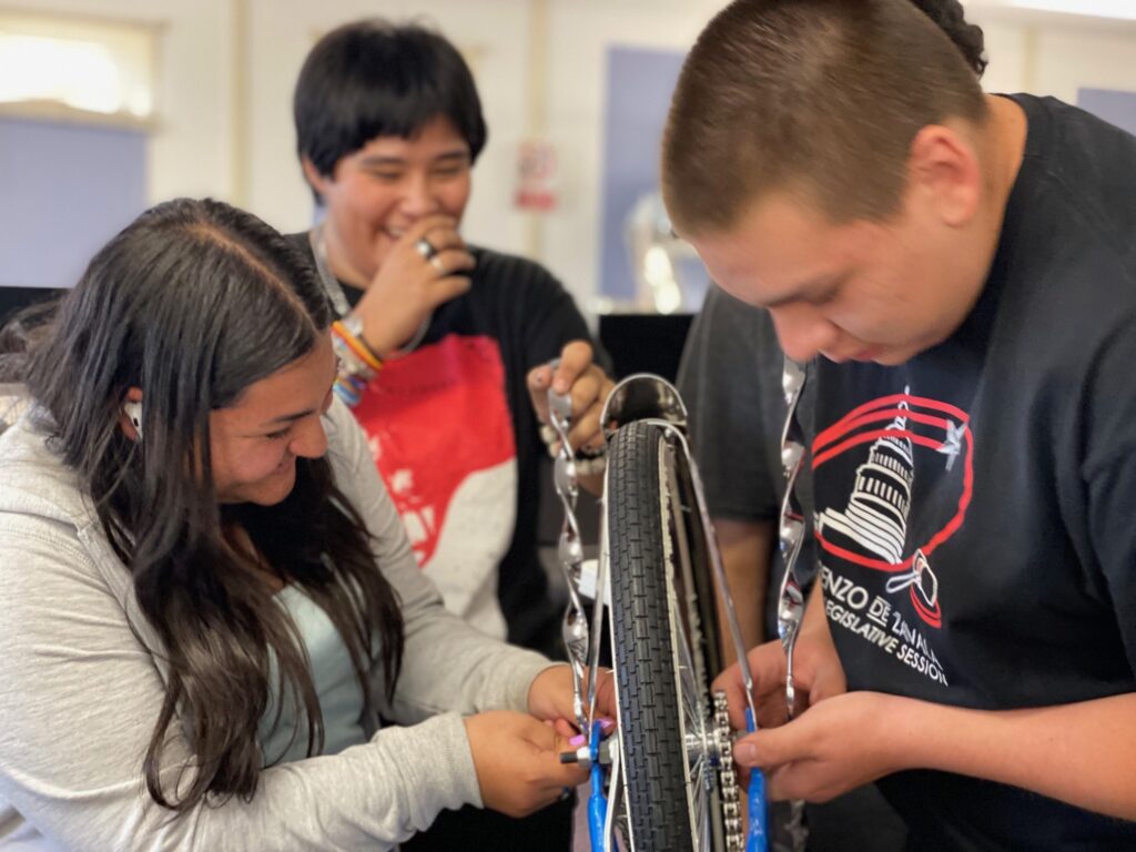 Four students in the Espanola Lowrider Bike Club work on transforming a blue bike tire in the shop.