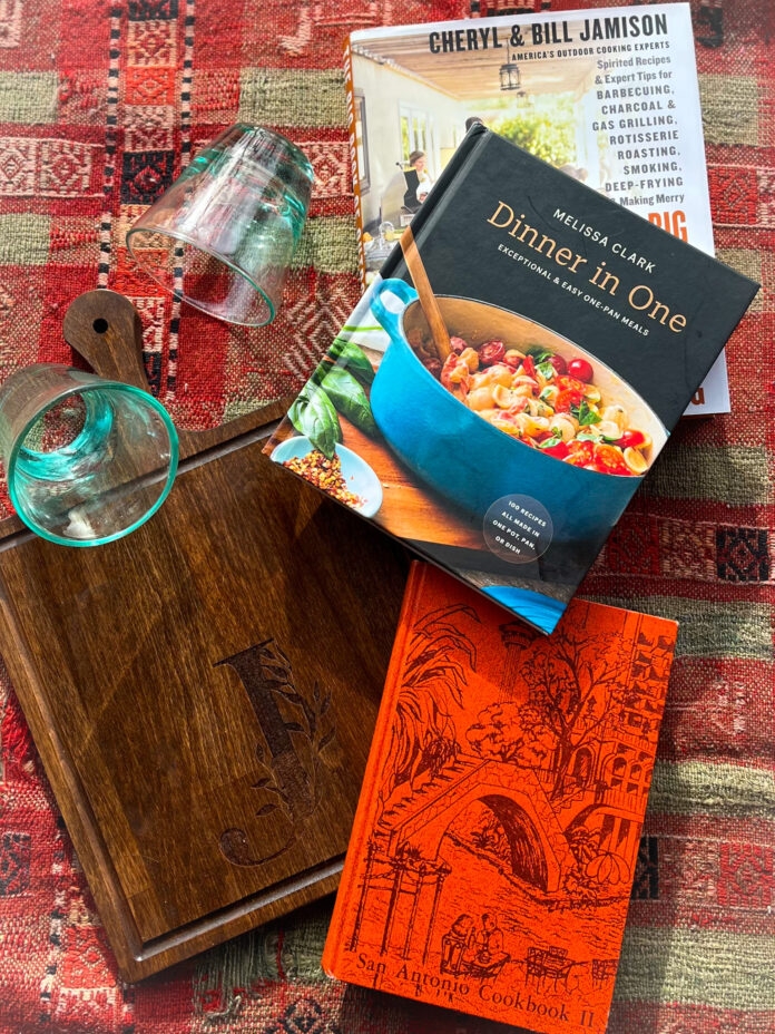 A red patterned blanket with cookbooks and kitchenware on top of it advertising items at Kitchenality.