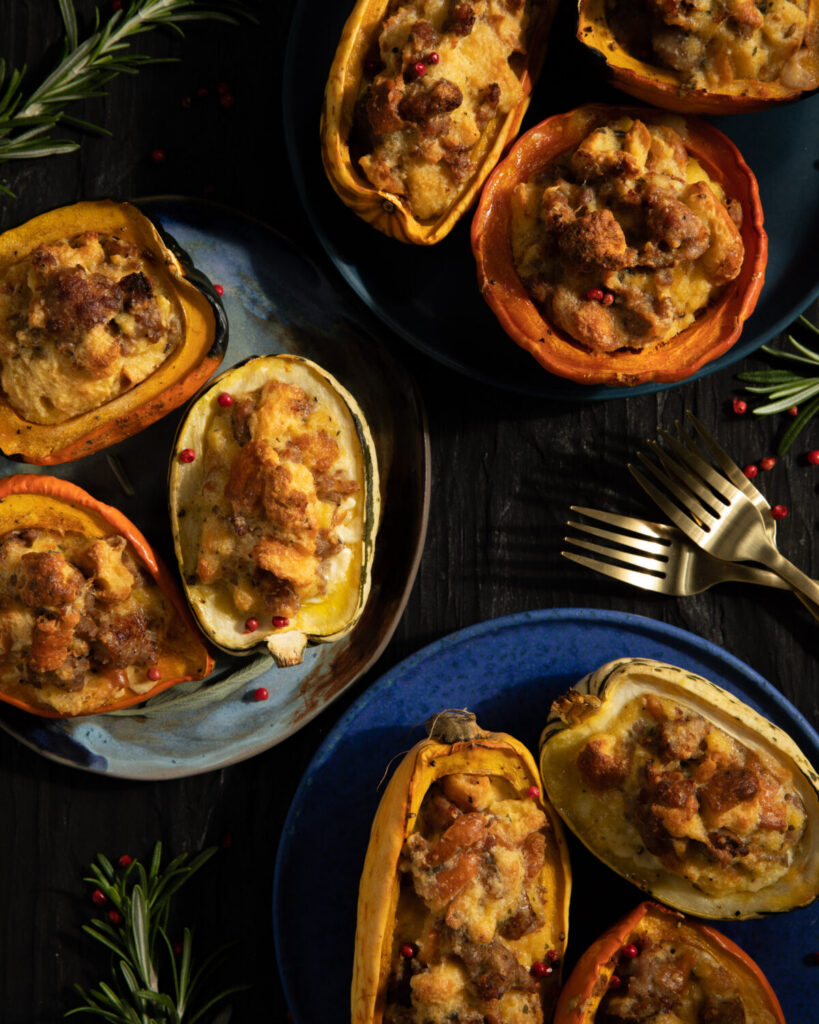 Three different shades of blue plates with bread pudding stuffed small halved squashed with rosemary and red peppercorn garnish around the plates