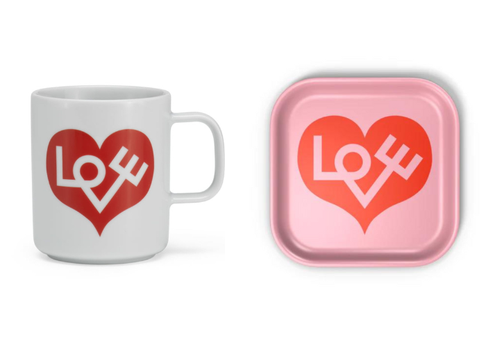 A white mug with a heart heart and the world love sits to the left of a pink tray with the same deisgn.