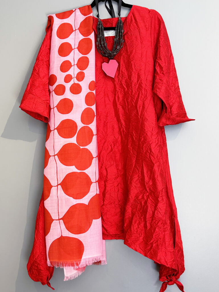 A red dress with a white scarf with red dots layerd over top and a pink heart by the neckline.