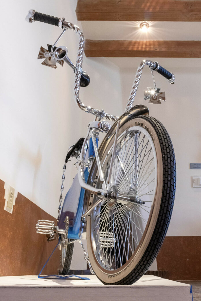 A blue bicycle made into a lowrider by the Espanola Lowrider Bike Club sits on a stand in the studio.