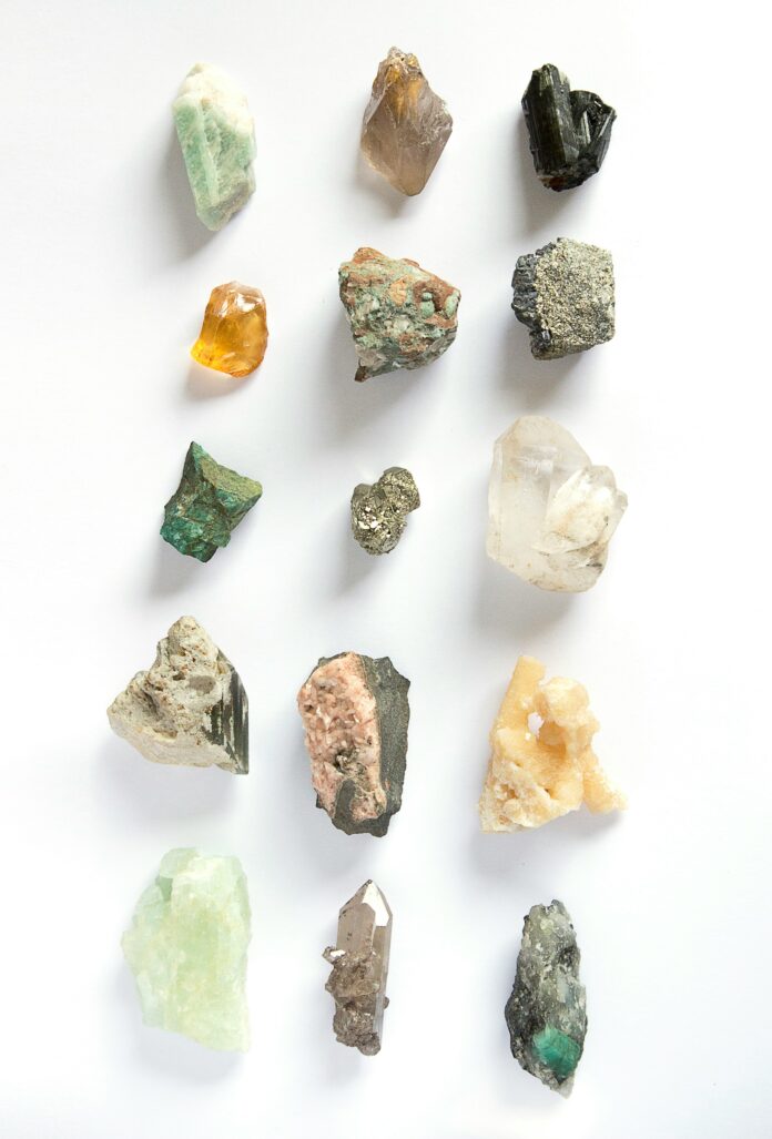 Different styled gems and rocks sit in a grid layout in various shapes, sizes, and colors advertising gem and mineral shows in New Mexico.