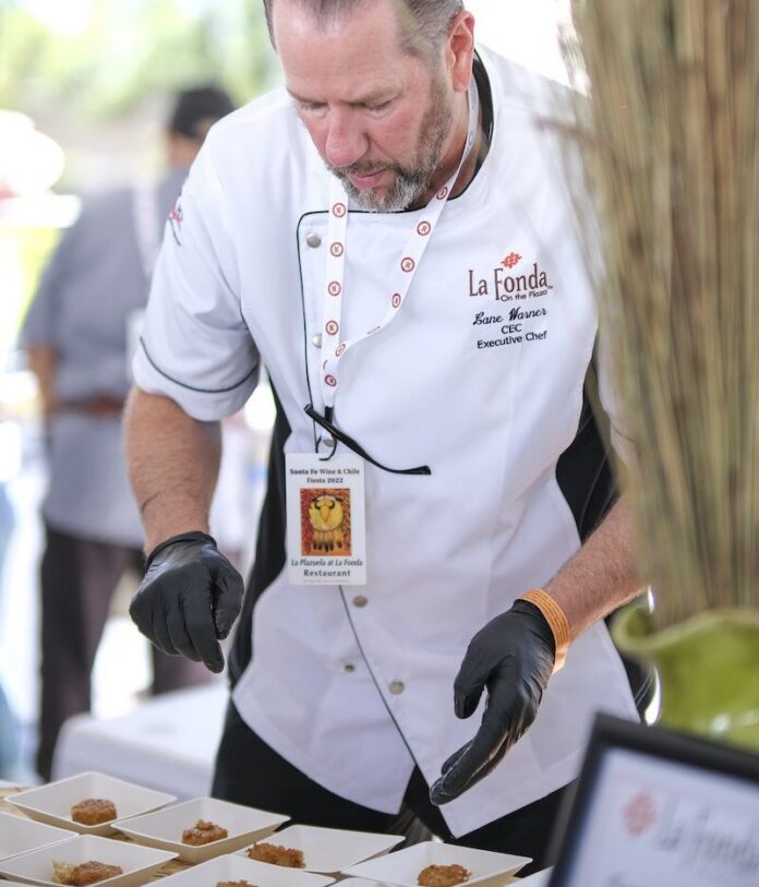 A man in a white chefs coat dresses small appetizers.