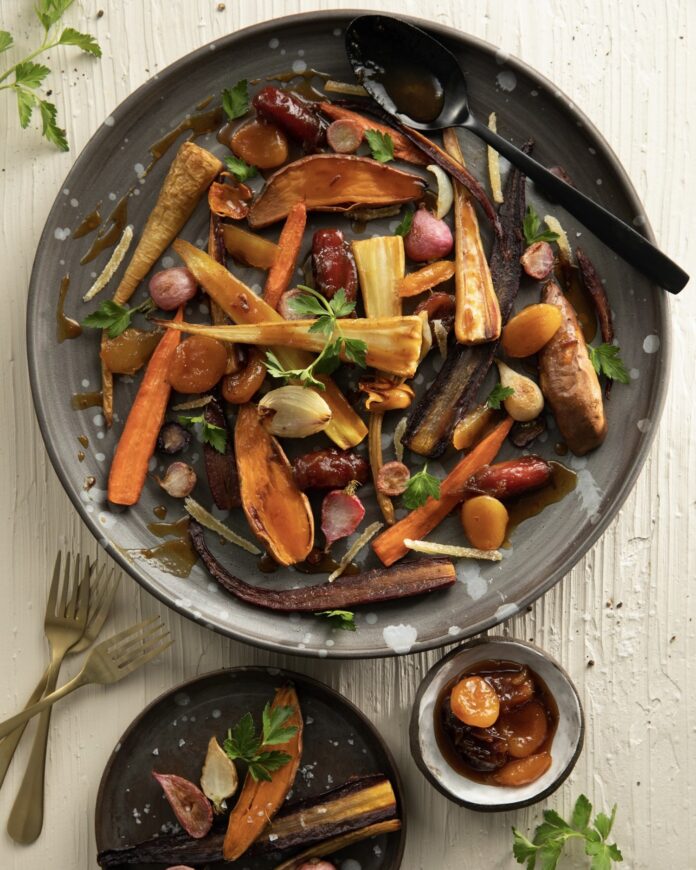 Tzimmes, a roasted root vegetable dish served in a large grey bowl with a dried fruit sauce.