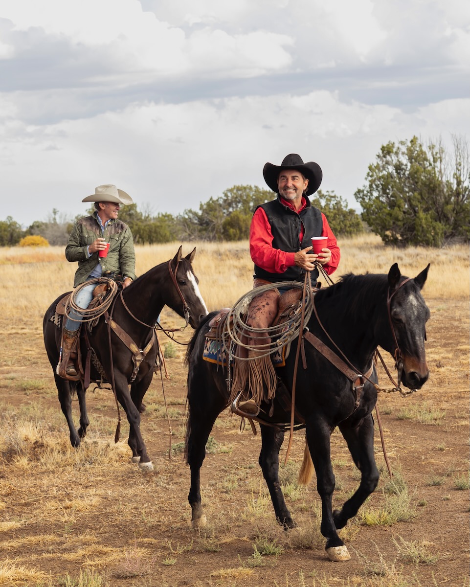 Two men in cowboy hats ride on two dark brown horses in the yellow grounds of Double DD Ranch.