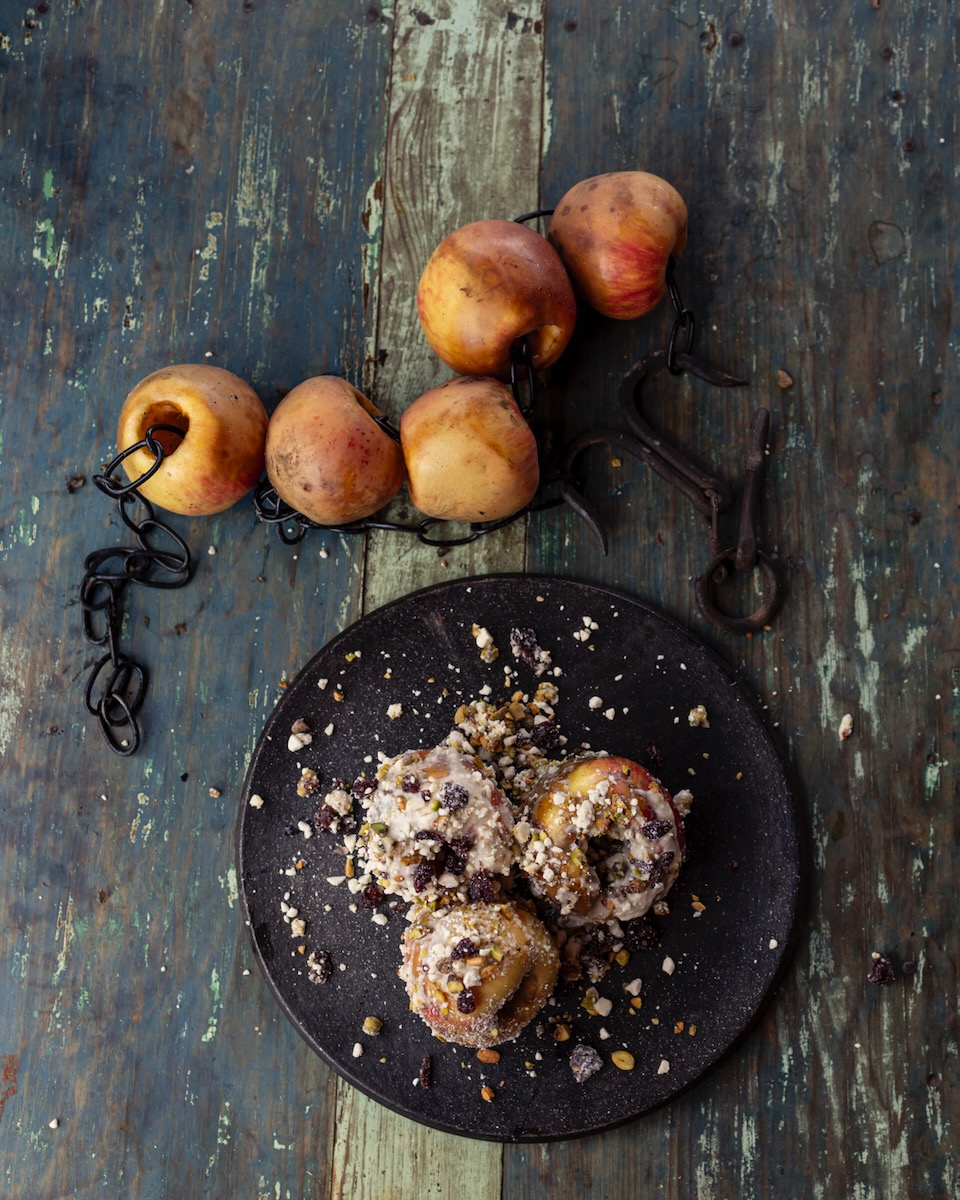 Three crispy apples sit in a pan on a table with others sit above uncooked.