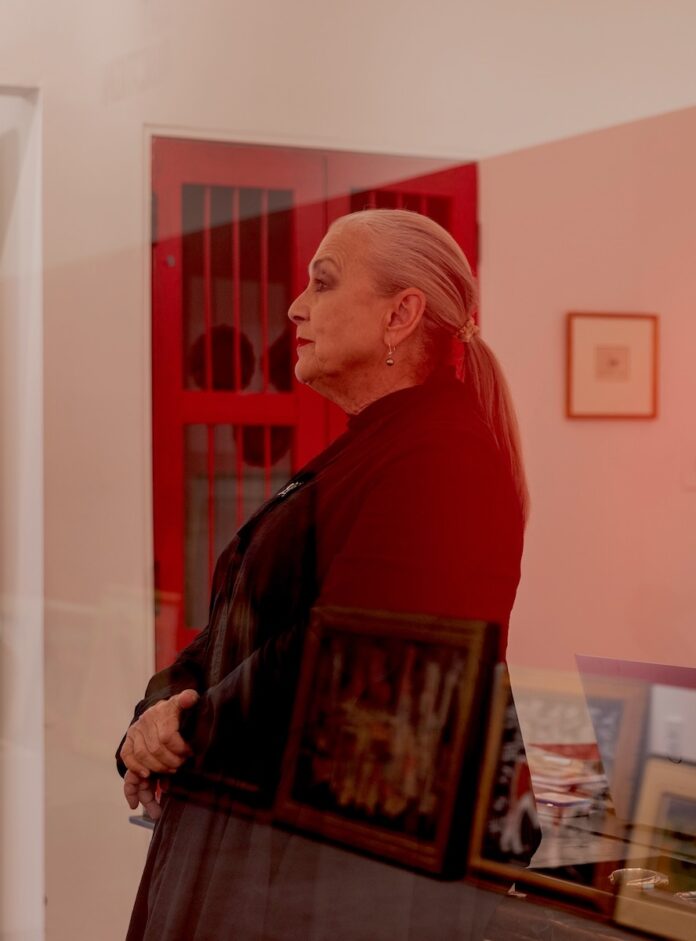 Gillian Blitch stands in a side profile, a long sleeve shirt with a ponytail down her back inside the Santa Fe Art Auction.