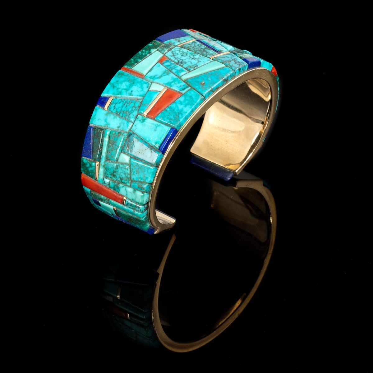 A ring sits on a black background with teal tiles and bits of orange plus a gold embellishment underneath.