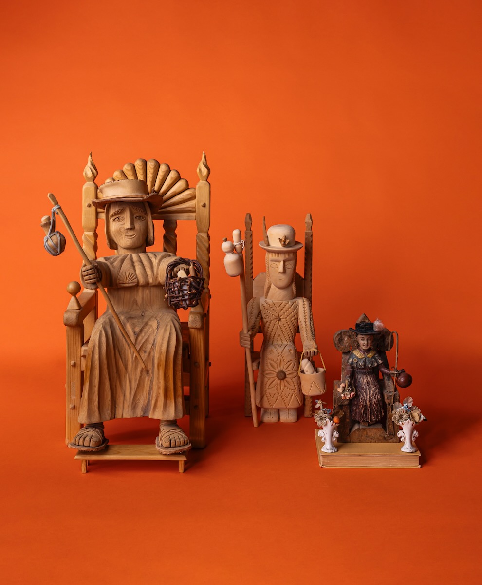 Three wooden sculptures of Santo Ninos figures sit in a line in different poses, all from the Spanish Colonial Society, against an orange background.