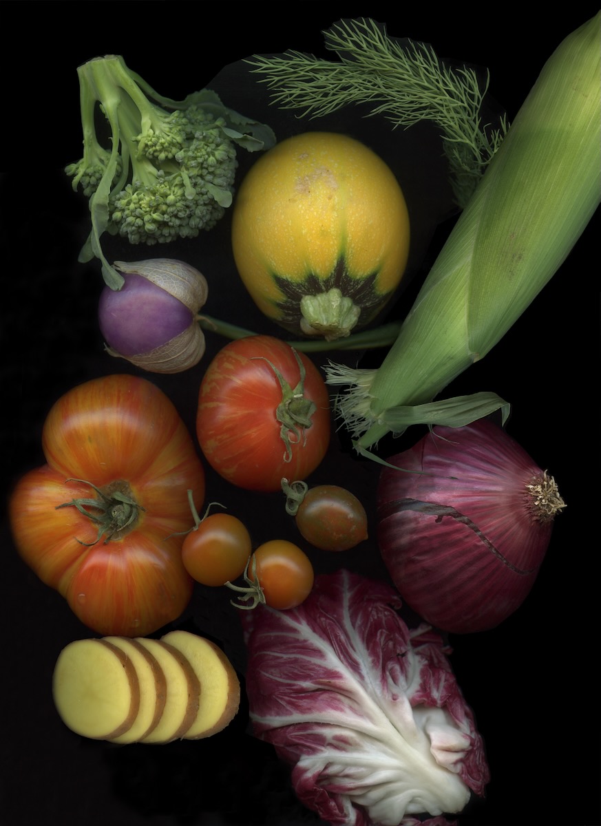 Colorful vegetables like tomatoes, purple cabbage, squash, broccoli, and corn from the Santa Fe Farmer's Market sit on a black background.