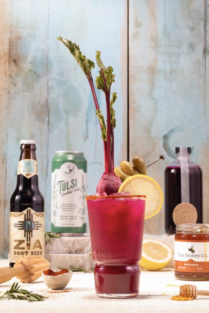 A red bloody mary cocktail with a radish sticking out of the top of the glass with the various ingredients in the background.