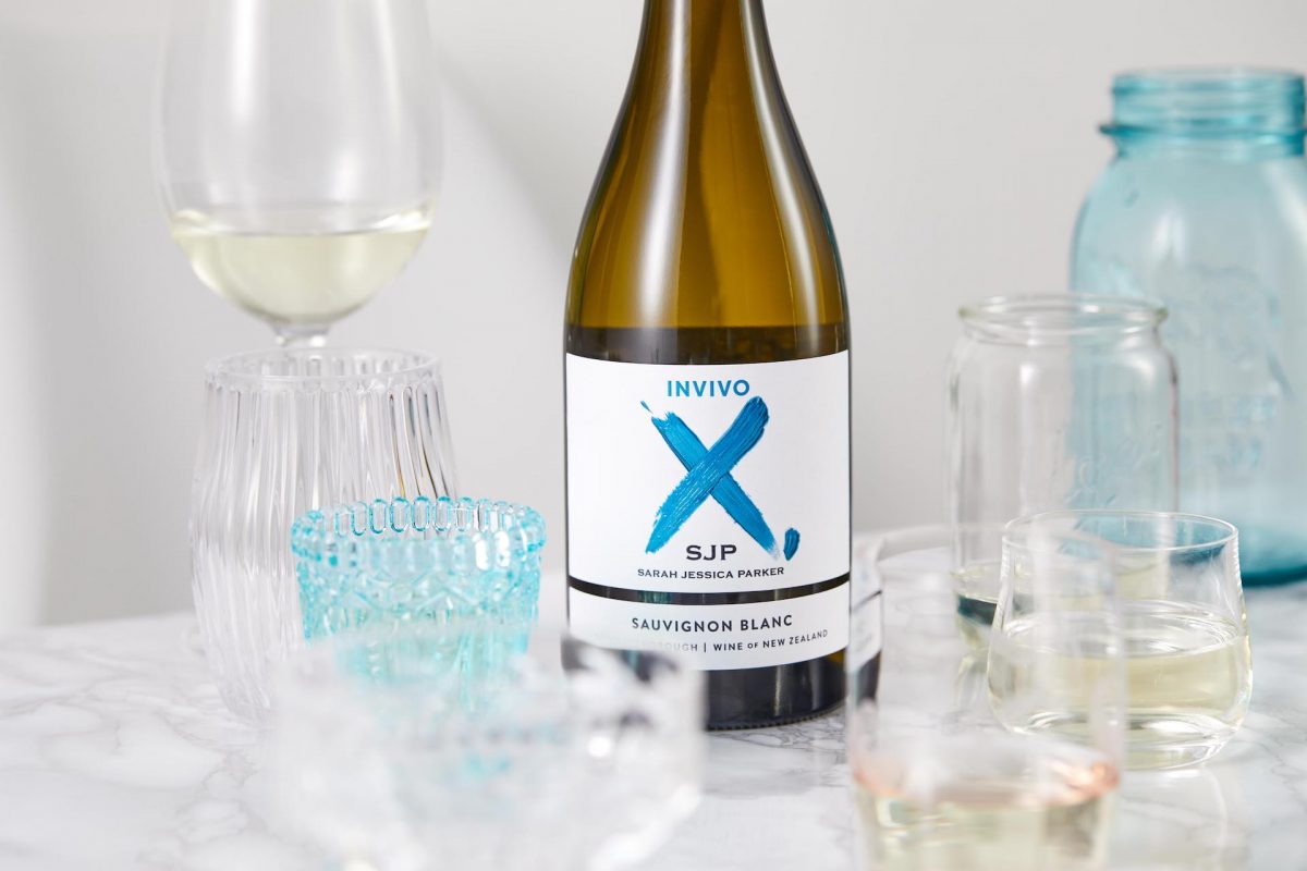 The bottle of a wine bottle with an X logo sits amongst various wine glasses in clear and opaque blue.