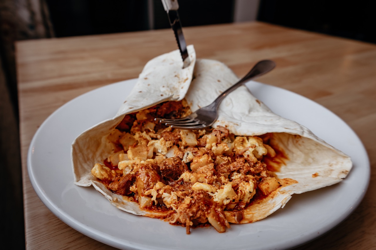 A tortilla is stuffed with grilled and seasoned shredded chicken spilling out on to a white plate.