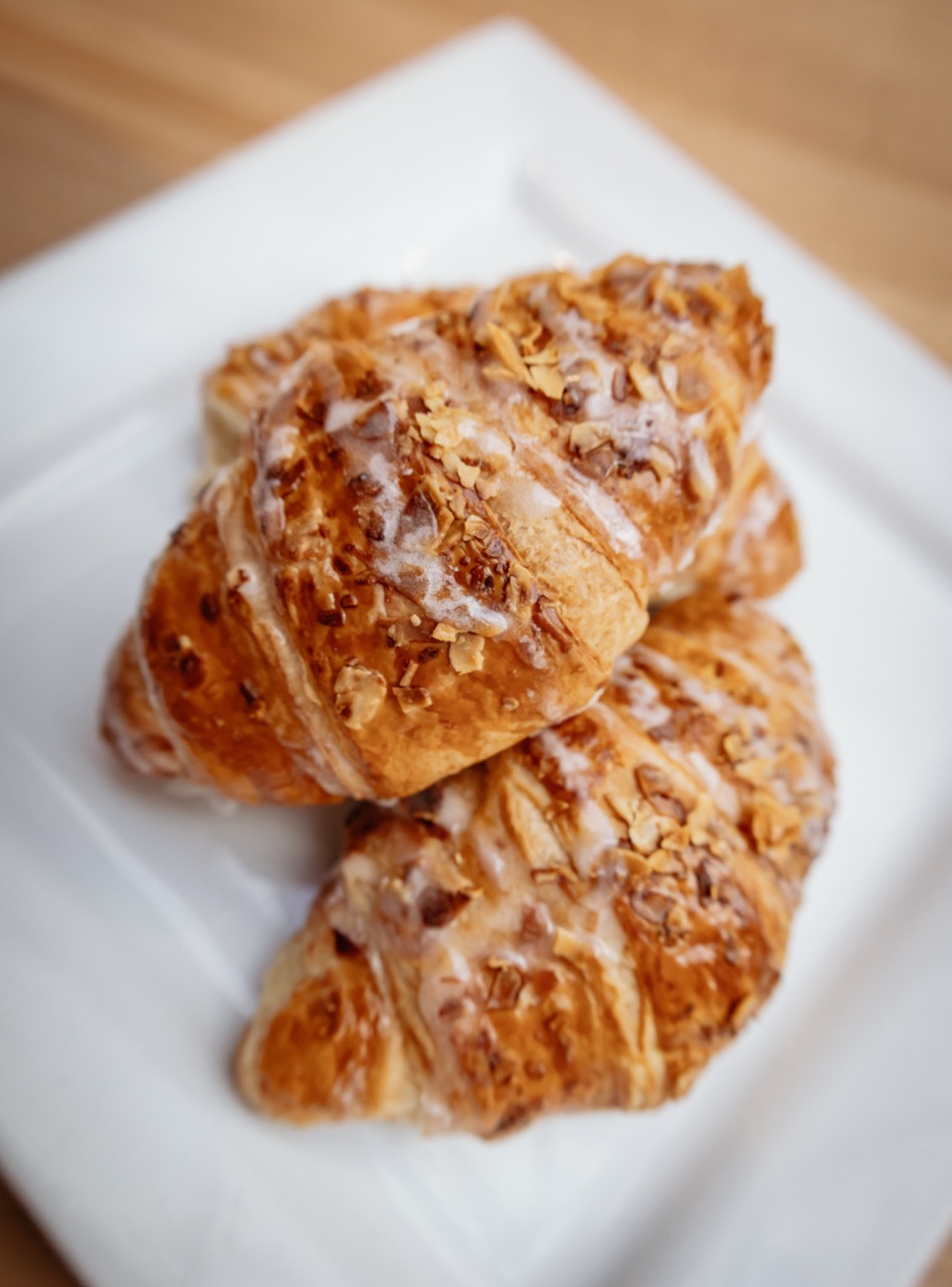 Three croissants with a nut topping sit on a white square plate.