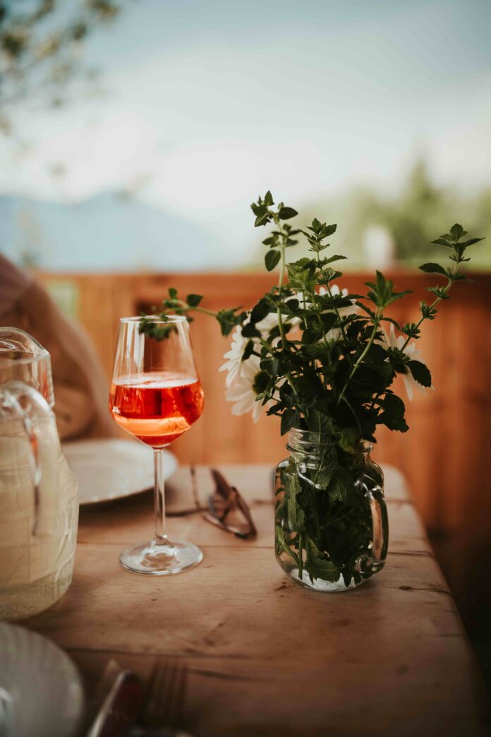 A wine glass sits on a picnic table next to a bouquet of greenery.
