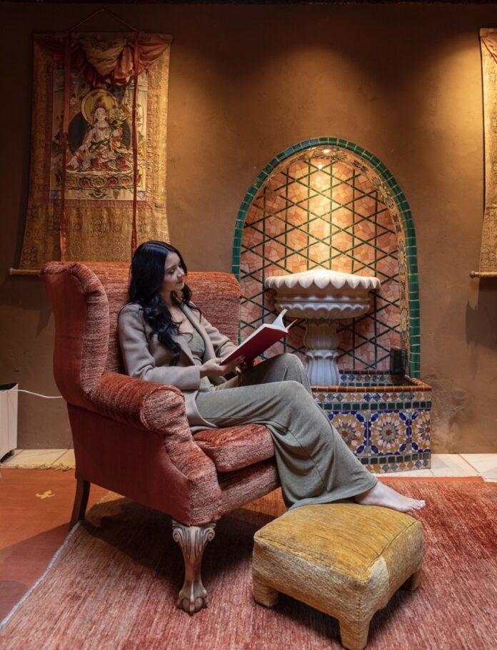 A woman sits in a red chair while reading a book with her legs crossed.
