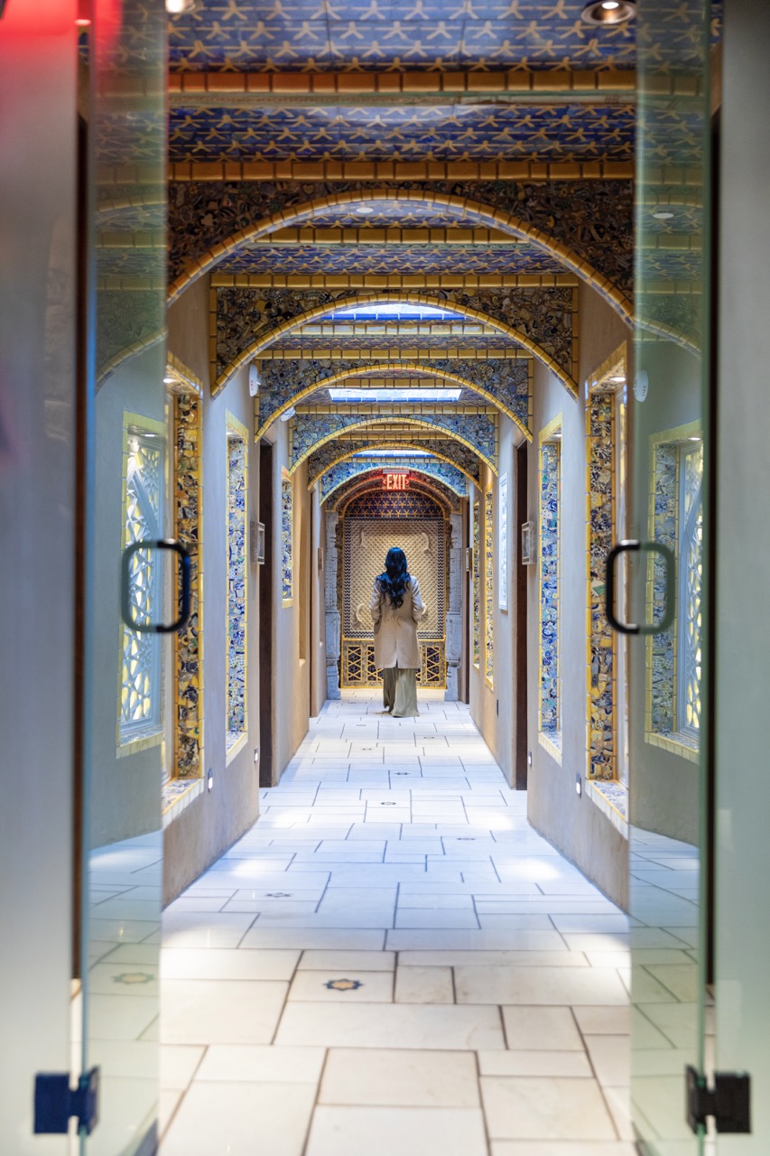 A woman walks down a long hallway with arches across the ceiling.