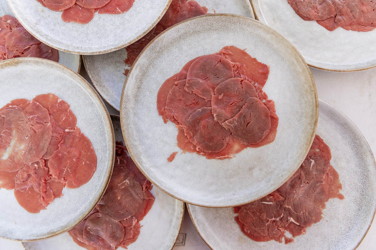 Charcuterie meats sit on white plates in pinkish red circles. 