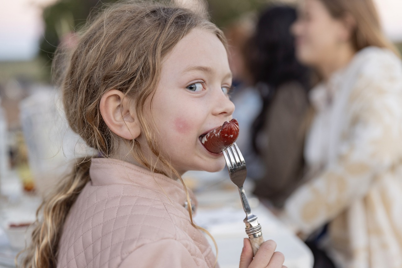 A little girl bites into a piece of food in a side profile pose. 