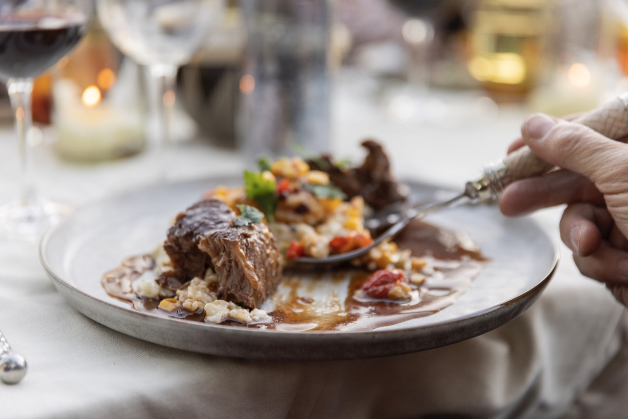 A plate holds a cute of meat and vegetables in a sauce on top of a dining table. 