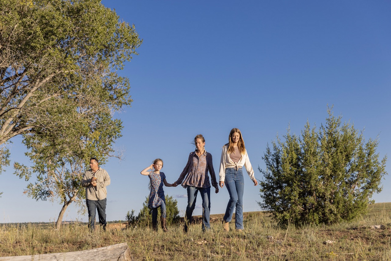 Four people walk down over a hill with trees on both sides of them. 