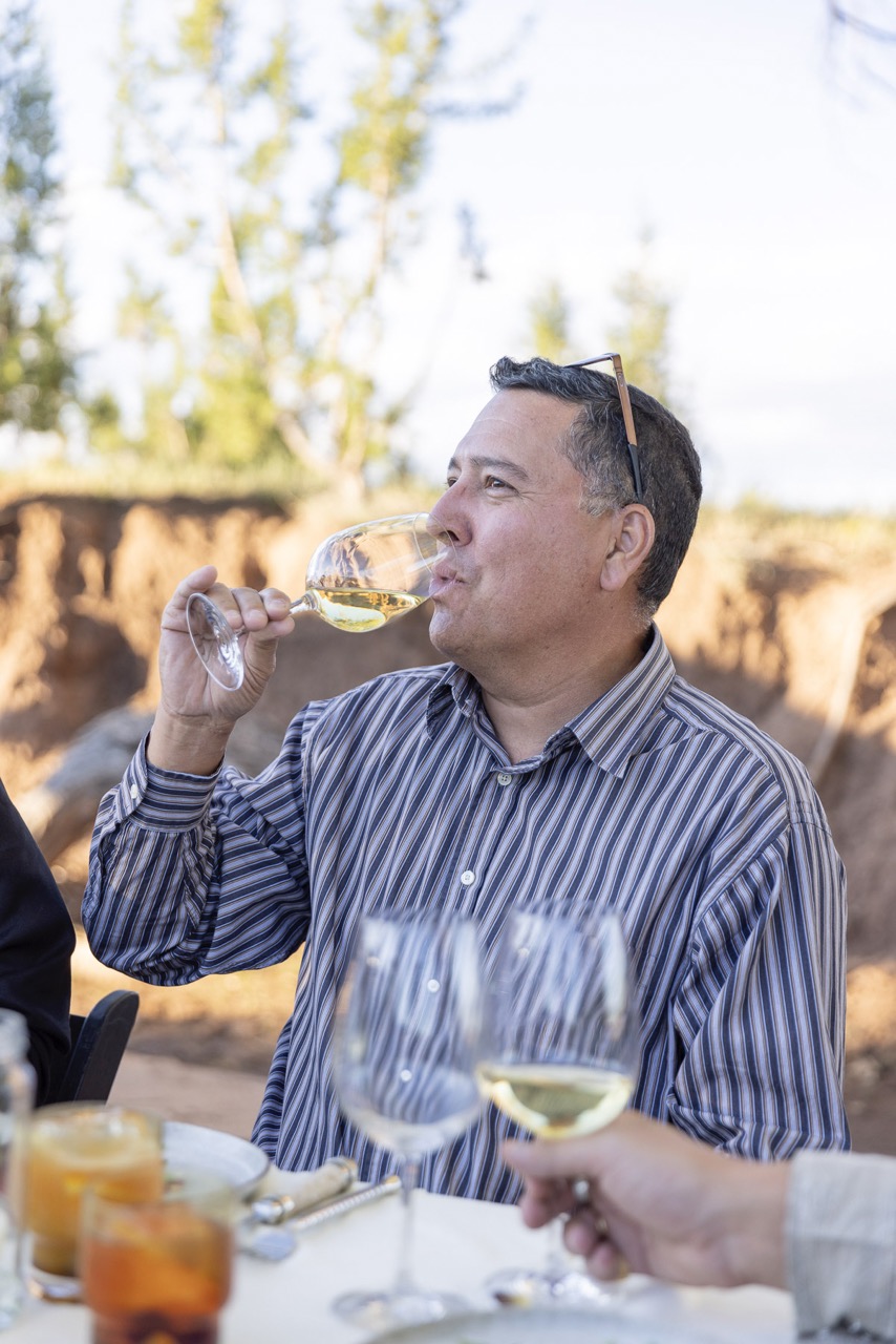 A man sips from a wine glass in a striped shirt. 