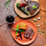 A mouthwatering grilled bone-in tomahawk steak, perfectly charred and served with sweet potato gratin, vibrant heirloom baby carrots, and drizzled with both green and red chile gastrique.