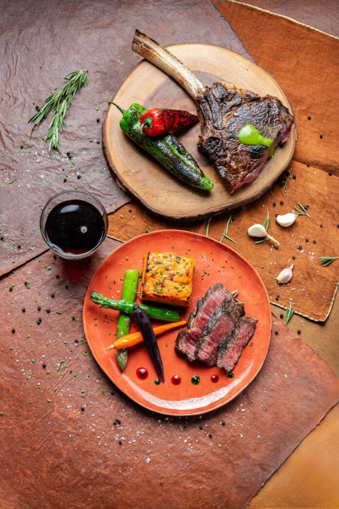 A mouthwatering grilled bone-in tomahawk steak, perfectly charred and served with sweet potato gratin, vibrant heirloom baby carrots, and drizzled with both green and red chile gastrique.