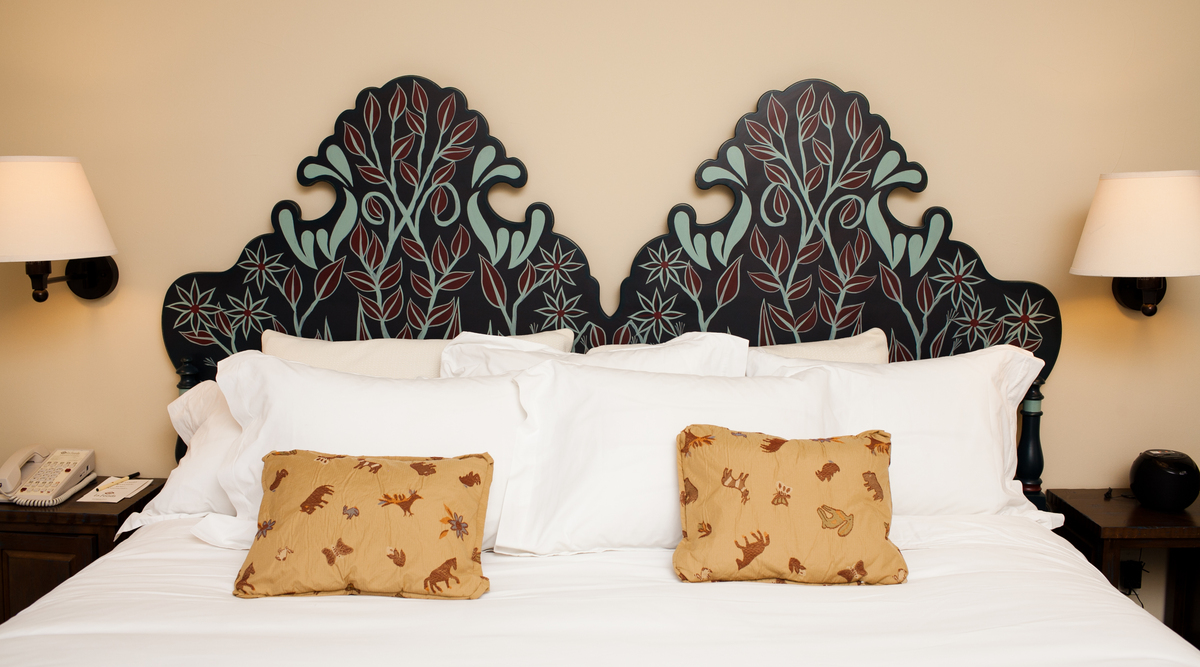 Decoratively painted hotel bedroom featuring an ornate leaf-patterned headboard surrounded by accent pillows and wall sconces, promoting a relaxing atmosphere.