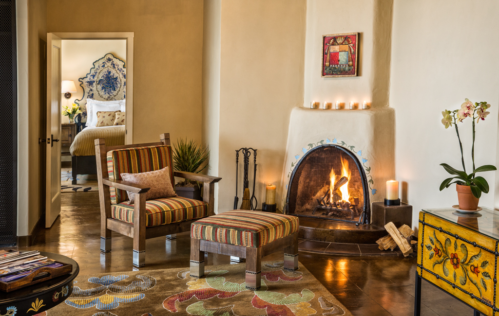 Tastefully decorated hotel living room featuring a cozy seating area with armchairs and ottomans surrounding a lit fireplace, promoting relaxation and comfort.