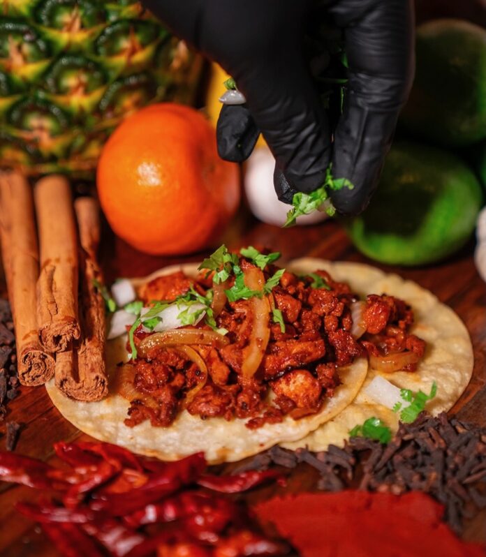 A Mexican tortilla sits on a red table with meat spread on top as a person sprinkles cilantro over the meat at a restaurant in Albuquerque.