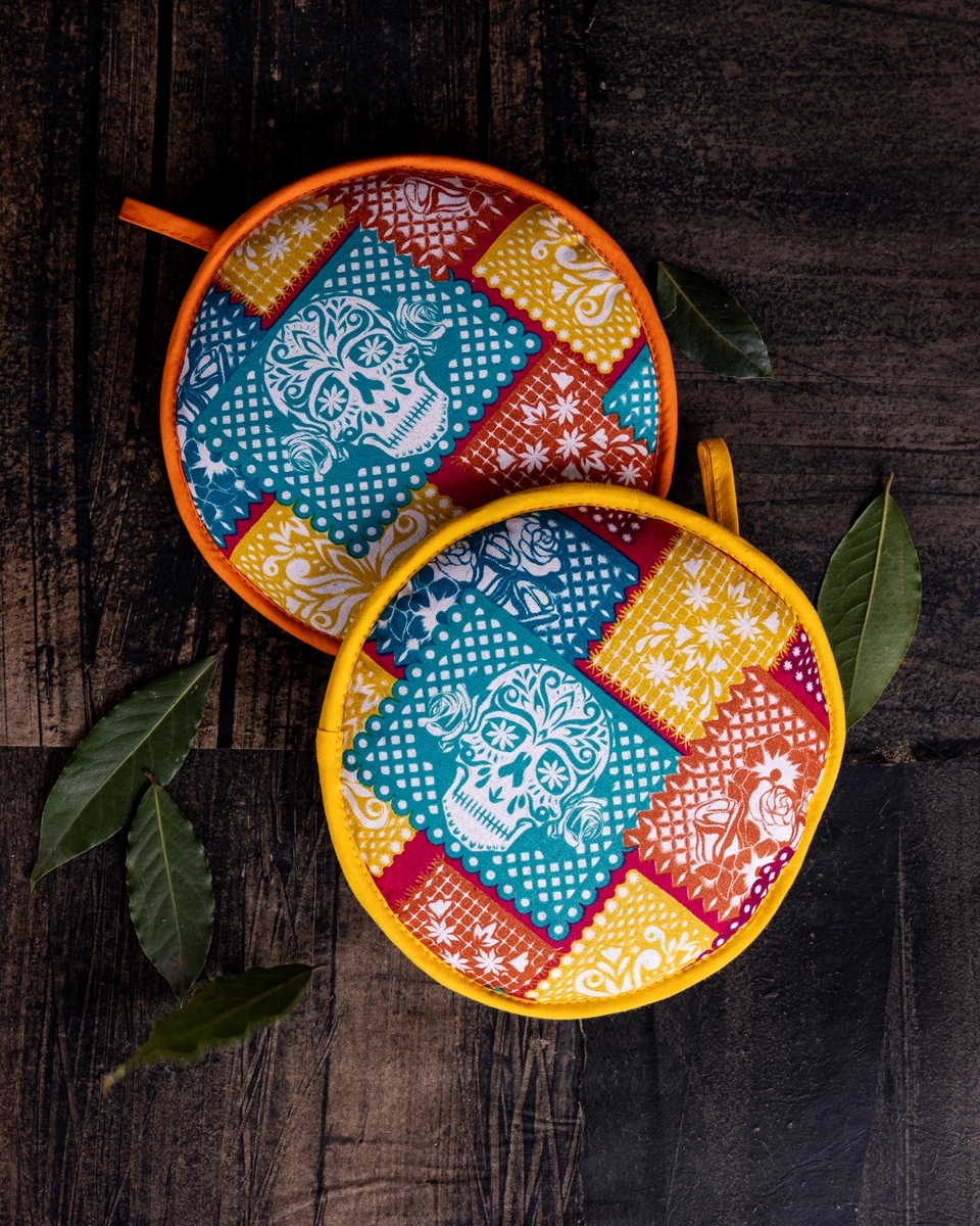 Arranged set of vibrantly patterned kitchen cloth potholders, oven mitts and dish towels displayed against a natural wooden surface, invoking themes of Southwestern cuisine, seasonal flavors and cultural heritage through their colorful designs.