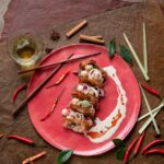 Gourmet seafood mille-feuille on a red plate, featuring crispy shrimp and calamari, garnished with herbs and sauces.