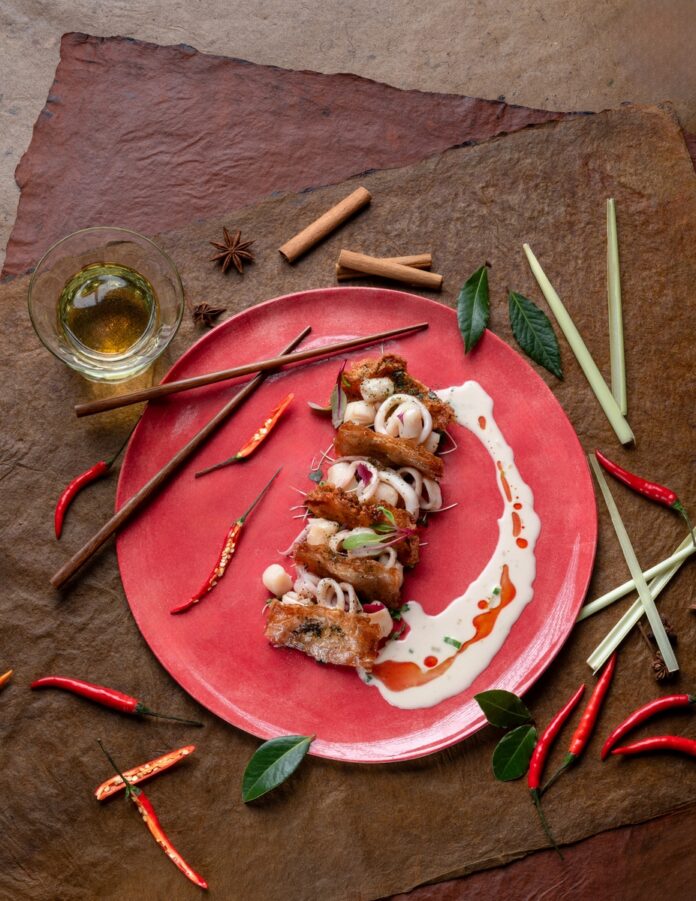 Gourmet seafood mille-feuille on a red plate, featuring crispy shrimp and calamari, garnished with herbs and sauces.