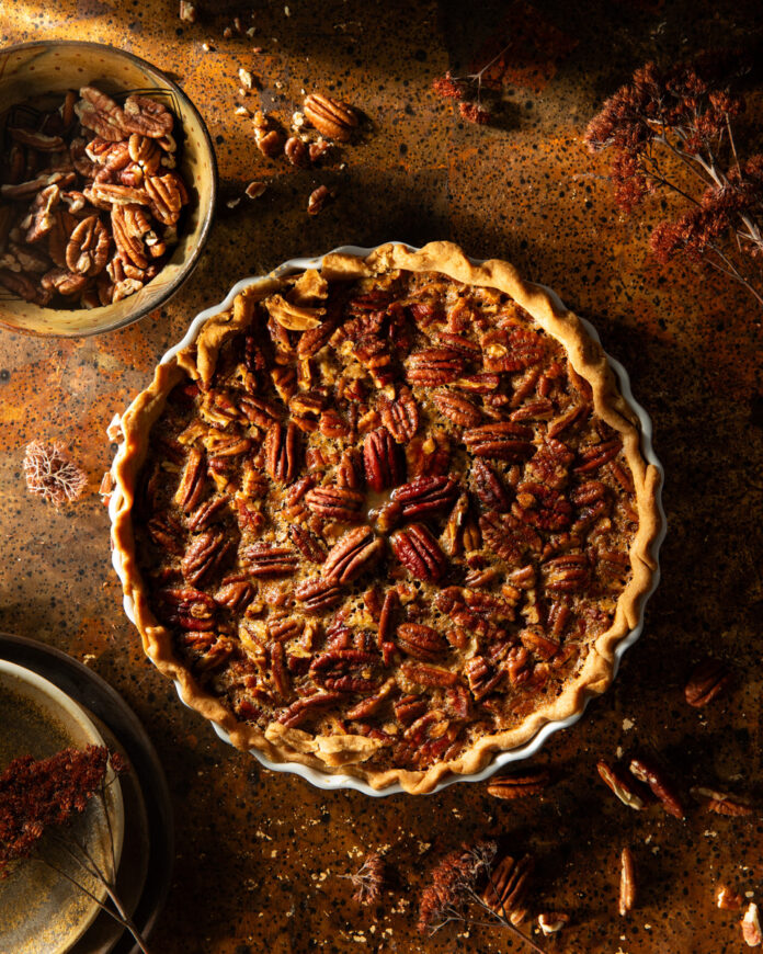 Freshly baked pecan pie with a golden brown crust and filling that is bubbling around the edges, showcasing the glistening texture of the sweet filling loaded with chopped pecans.