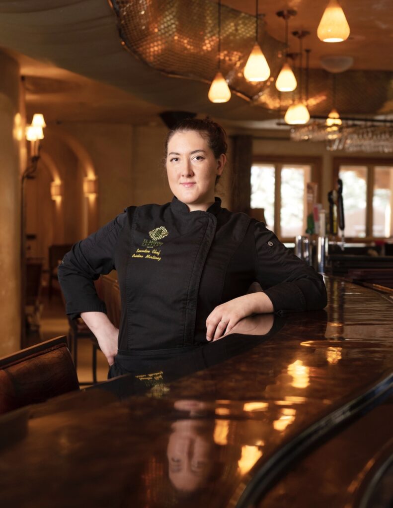 A Winter Staycation at El Monte Sagrado A woman chef stands in all black at a wooden bar.