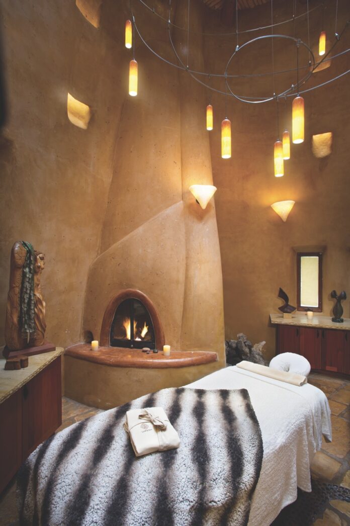 The spa room at El Monte with a white bed, curvy fireplace, and warm lights.