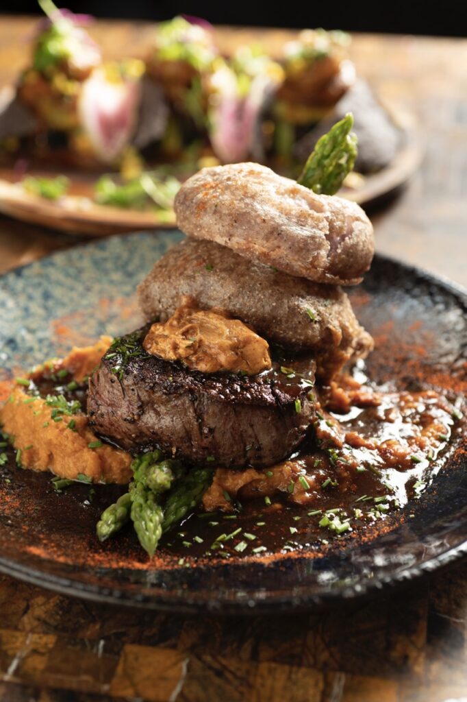 A Winter Staycation at El Monte Sagrado A piece of steak with blue corn onion petals sits on a blue plate.