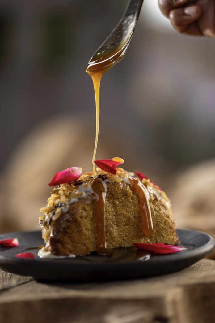 A corn dessert shell holds ice cream with rose petals and caramel drizzling down from a spoon above it at The Mystic Santa Fe.