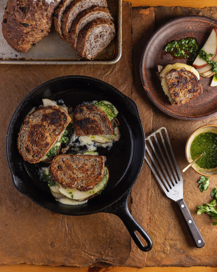 A pear grilled cheese sandwich set on a rustic table with slices of bread beside it