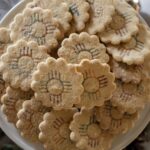 A pile of flower-shaped biscochitos are arranged in a circular shape.