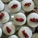 A table full of blue corn macarons with a red floral decoration on top of each.