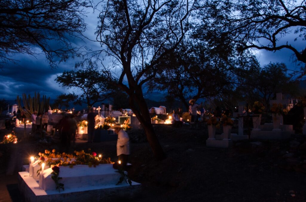 A group of people gather in the dark for Day of the Dead in Mexico with candles surrounding graves.