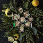 A small pile of Lemon Ricotta Cookies sit on leaves of greenery with lemon peels scattered throughout.