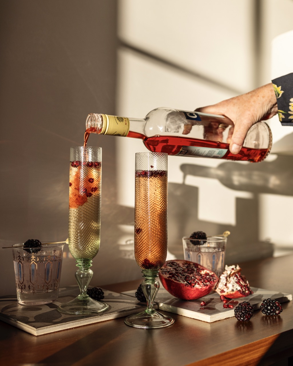 A person pours Campari into a Pomegranate Prosecco Cocktail in a champagne flute.