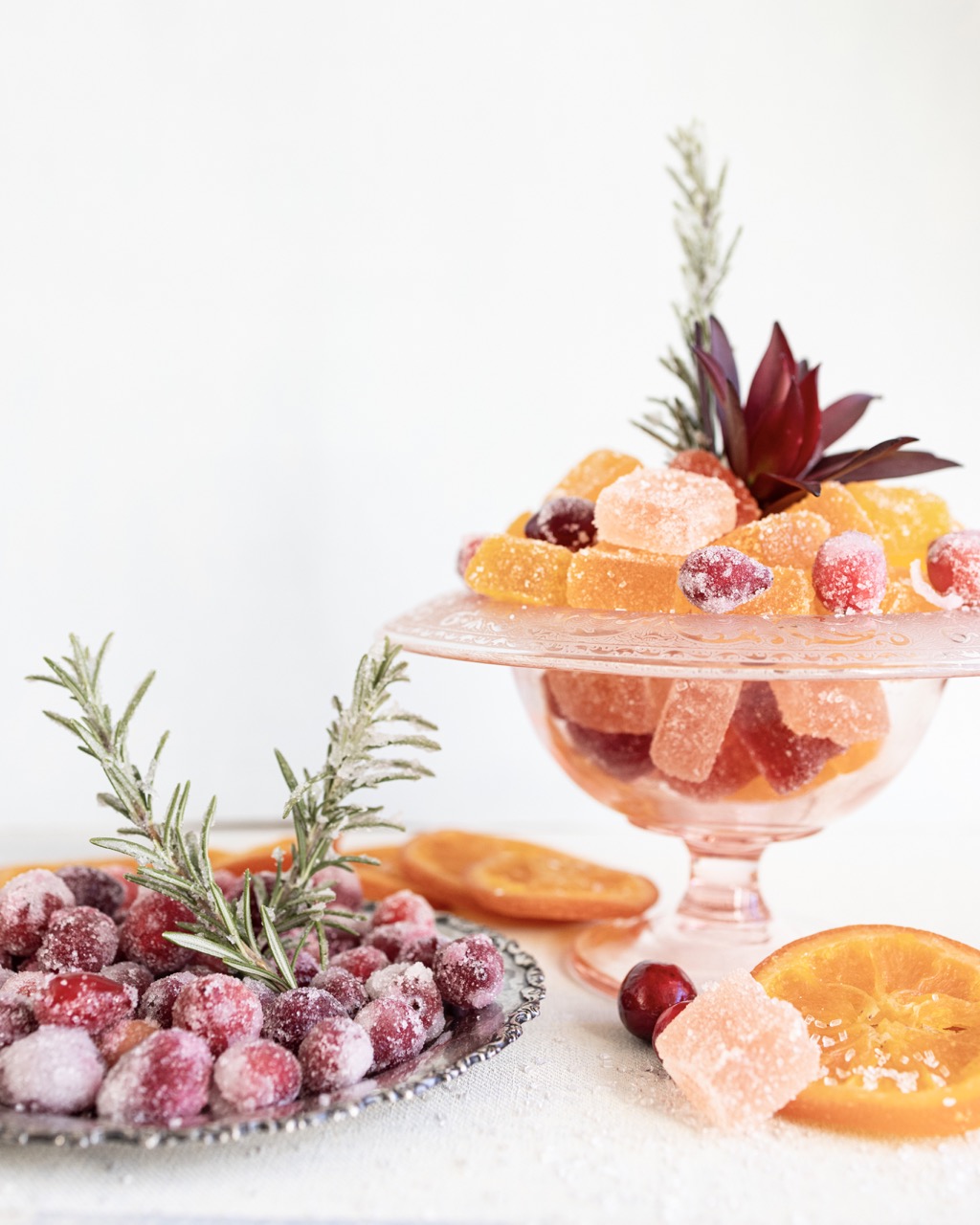 On a platter and glass plate sit pieces of apricot candy and desserts with sprigs of rosemary in them.