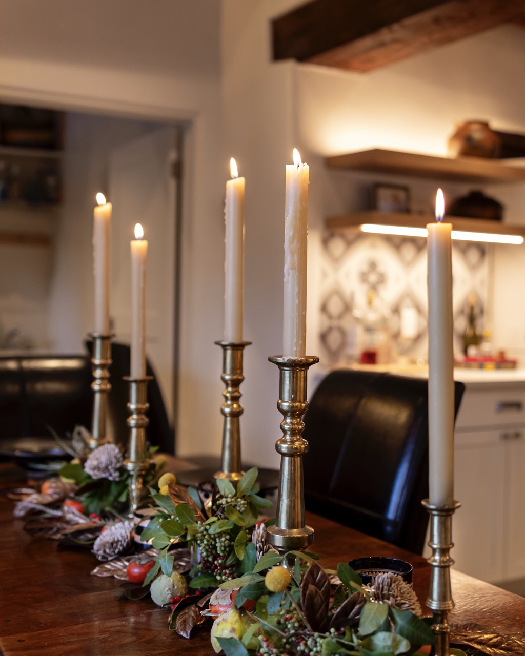 Antique candlesticks with lit candles on them sit on a long brown dining table.