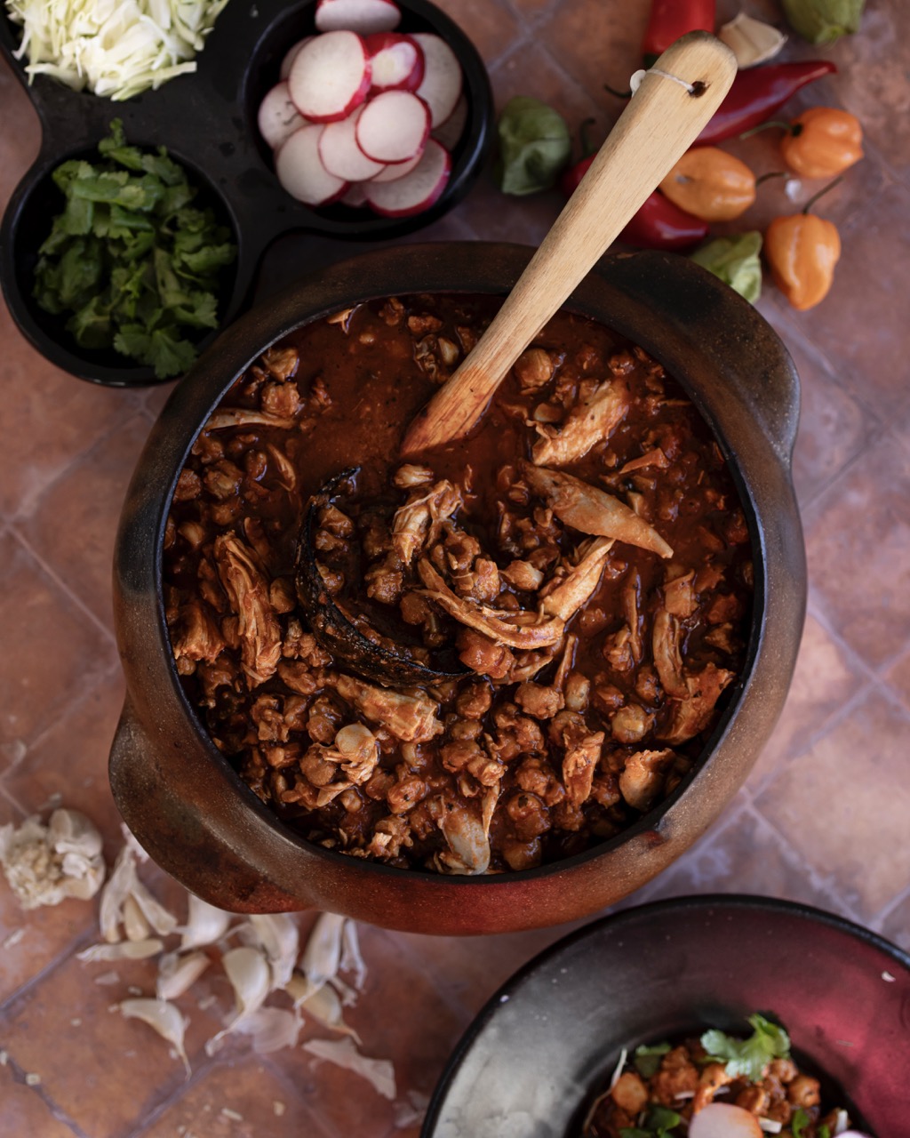 A red pot of stew sits by various bowls of chopped vegetables.