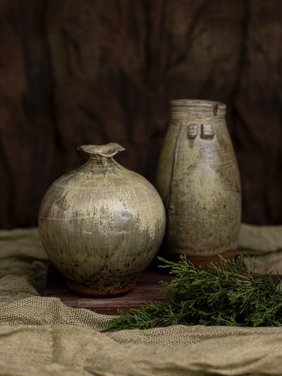 Two ceramic pottery vases that have an old look to them. One is bulbous while the other is a taller vase.